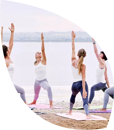 Grupa kobiet ćwiczy jogę na plaży. Ćwiczenia są dobre na stres, tak samo jak regularne stosowanie leków z magnezem.
