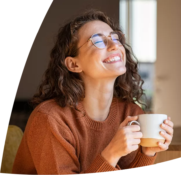 Uśmiechnięta kobieta z kubkiem kawy w ręku, lek OTC Magne B6 Forte pomaga uzupełnić poziom magnezu w organizmie.