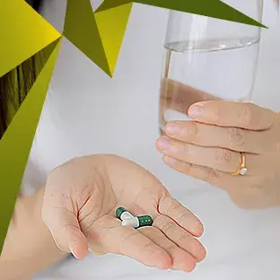 Zbliżenie dłoni kobiety ze szklanką wody i dwiema kapsułkami Essentia Proactive, który proaktywnie wspomaga zdrowie wątroby.