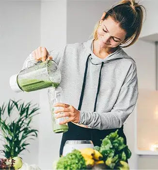 Kobieta w kuchni nalewa zielone smoothie do bidonu; również suplement diety Essentia Proactive proaktywnie wspomaga wątrobę na co dzień.
