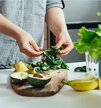 Zbliżenie rąk kobiety w kuchni, która przygotowuje smoothie; dieta dieta oczyszczająca wątrobę jest bogata w warzywa i owoce.