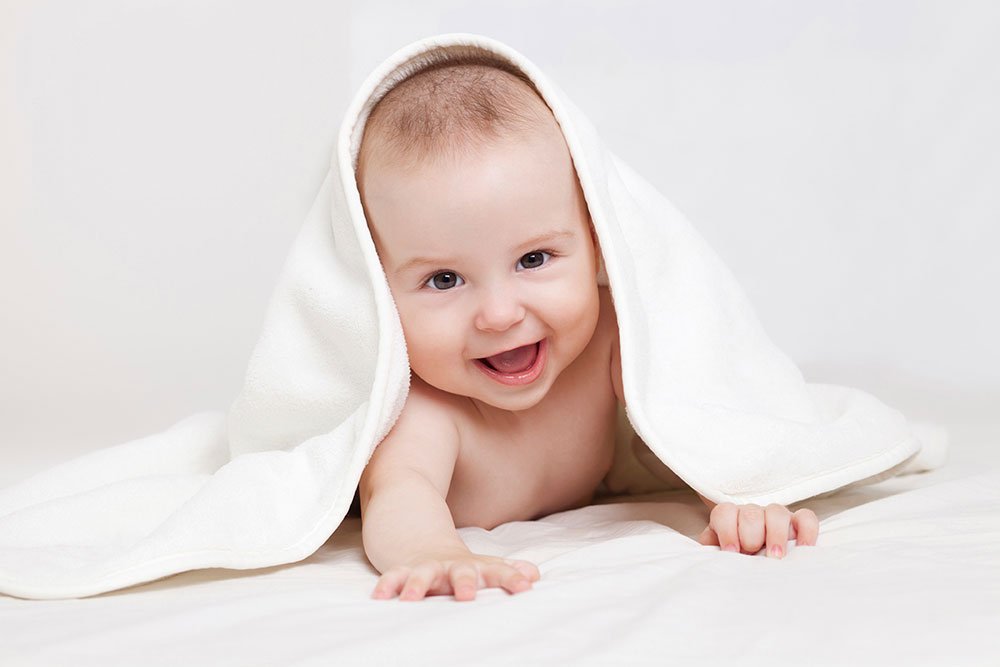 STE Baby under a white blanket smiling